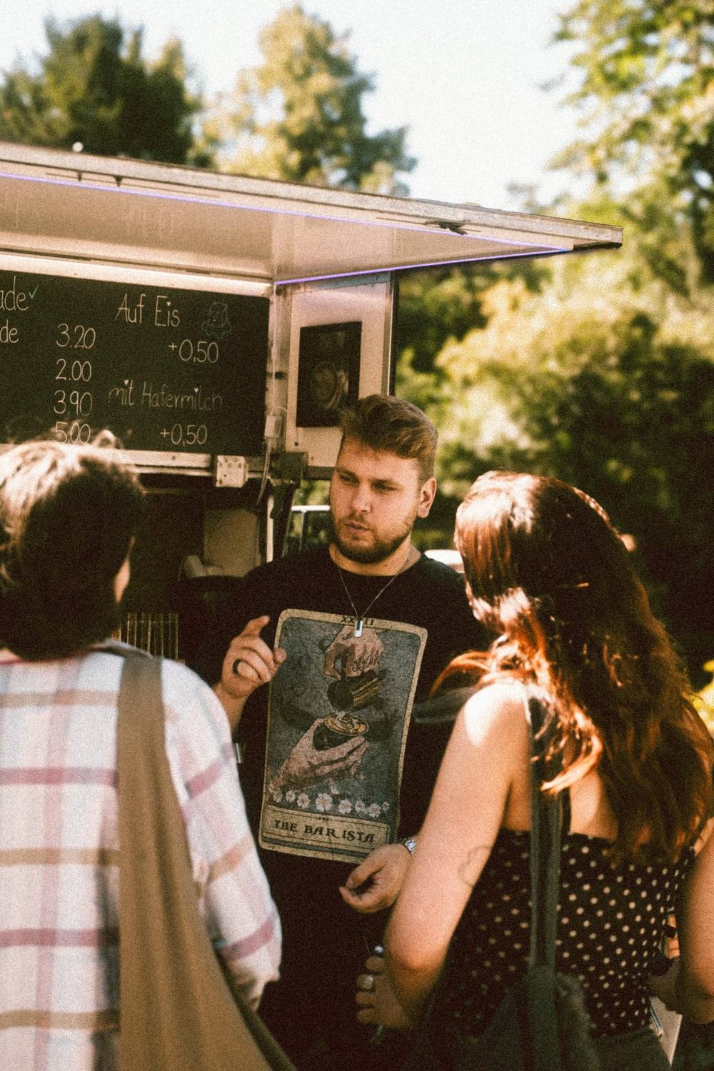 Barista zeigt Gästen die Kaffeekarte am Kaffeewagen